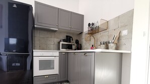 Una cucina compatta con pensili grigi, un frigorifero nero, un forno a microonde e un piano cottura.
