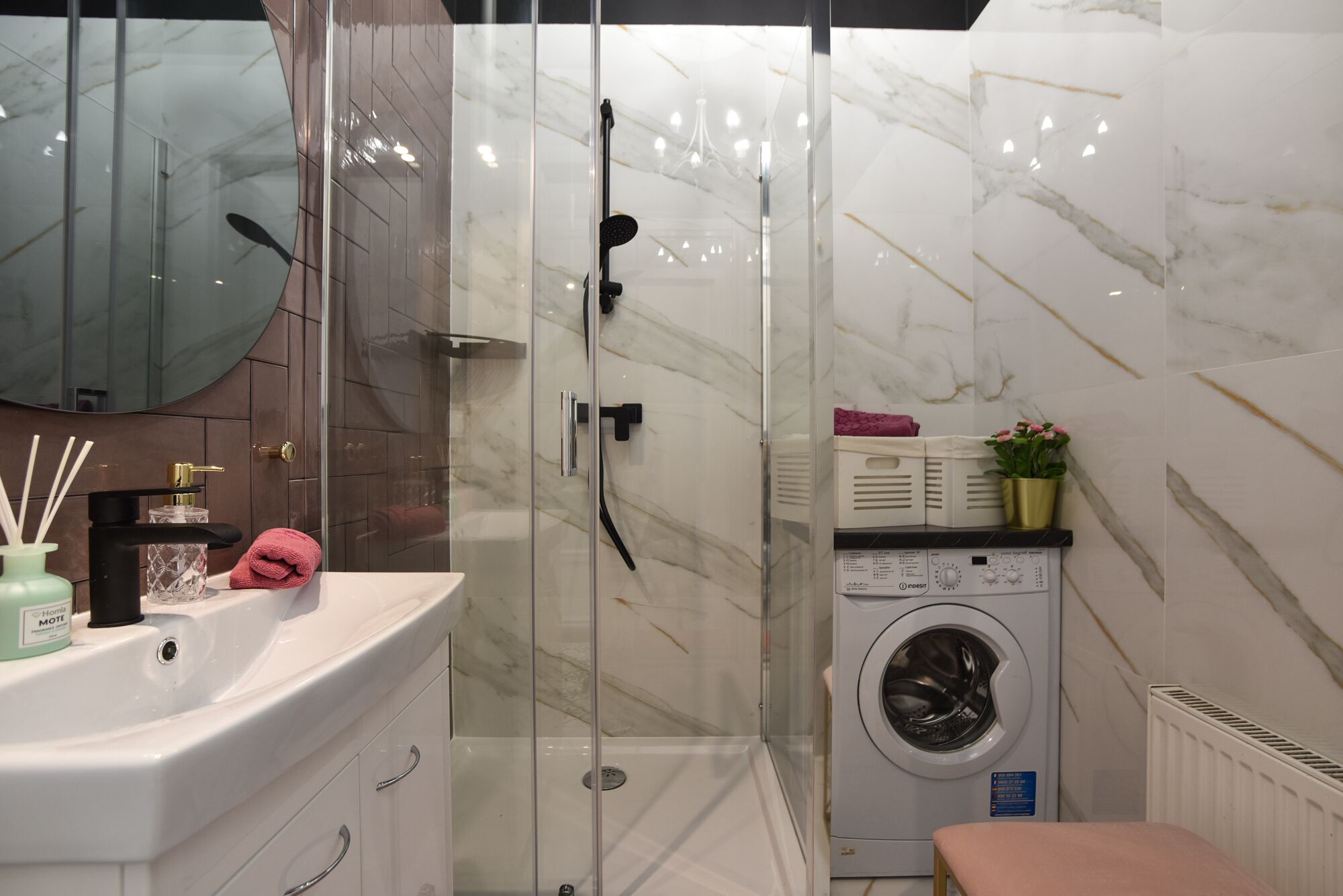 A modern bathroom with a glass shower enclosure, a built-in washing machine, and a vanity with a mirror.