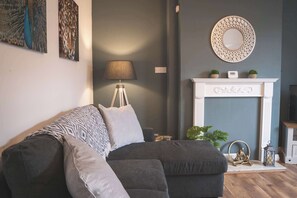 A living room with a grey sofa, a lamp, a fireplace, and wall art. - Spacious Home, Ideal For Families, FREE Parking! (Chester)