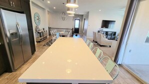A modern kitchen with a large island, stainless steel appliances, and a dining area with a long table and chairs. - Fully Equipped Vacation Home in Paradise Village (Santa Clara)