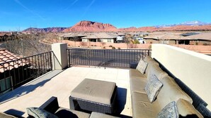 An outdoor patio with a sofa and ottoman, a metal railing, and a view of mountains in the background. - Fully Equipped Vacation Home in Paradise Village (Santa Clara)