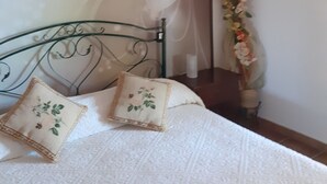 A bedroom with a bed, decorative pillows, a wall with a floral pattern, a mirror, and a vase with flowers. - Nature and relaxation (Sicilia)