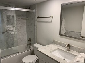 A modern bathroom with a glass-enclosed shower, a white toilet, a marble sink, and a large mirror. - Updated unit with sunset & beach view (Marco Island)