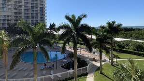 A resort with a swimming pool, palm trees, and a view of the ocean. - Updated unit with sunset & beach view (Marco Island)