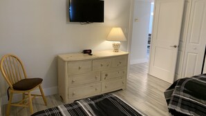 A bedroom with a bed, a wooden chair, a dresser, a lamp, a TV, and a door. - Updated unit with sunset & beach view (Marco Island)