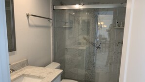 A modern bathroom with a glass-enclosed shower, a white toilet, and a marble countertop. - Updated unit with sunset & beach view (Marco Island)