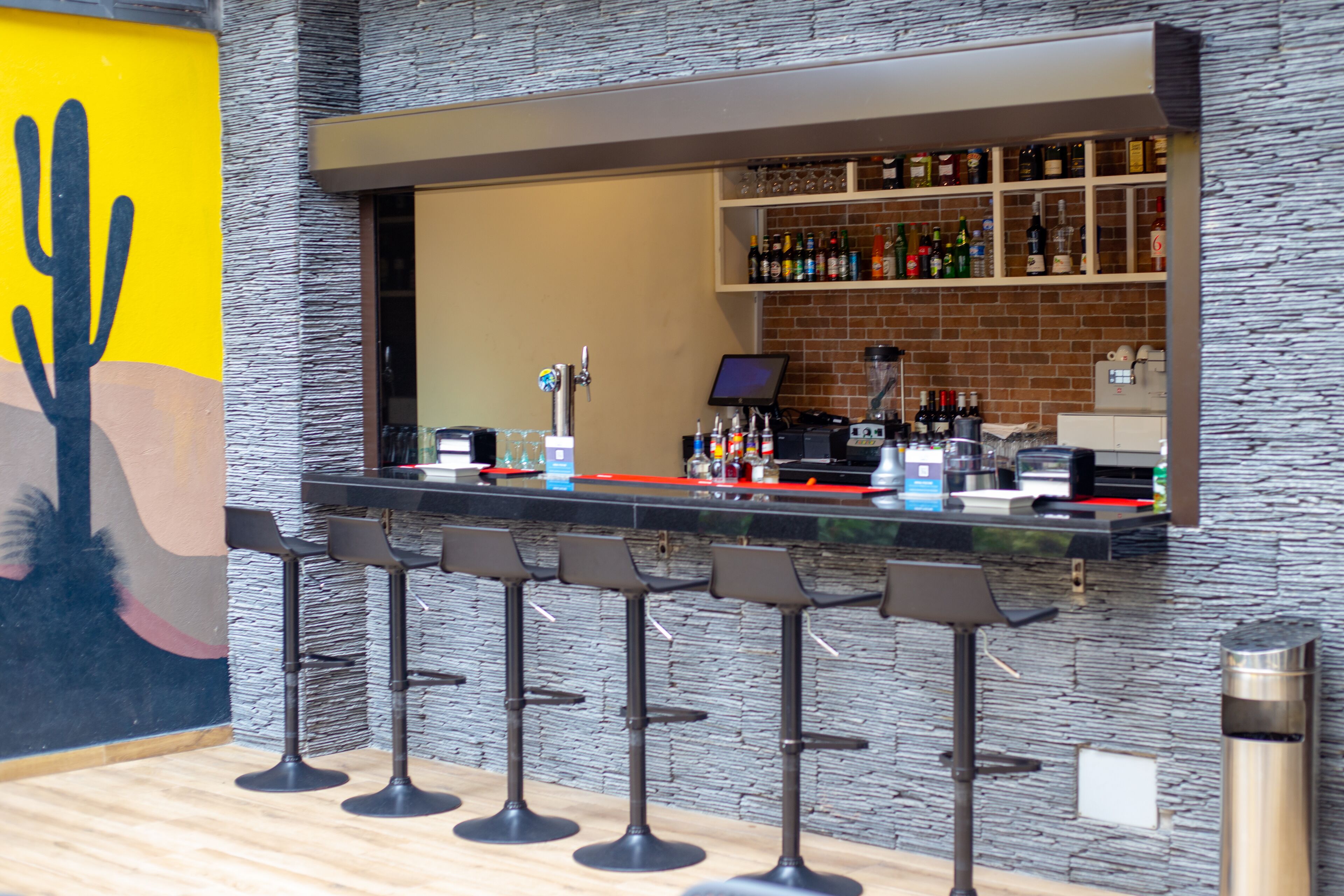 A bar area with a stone wall, a cactus mural, and a variety of bottles on shelves.