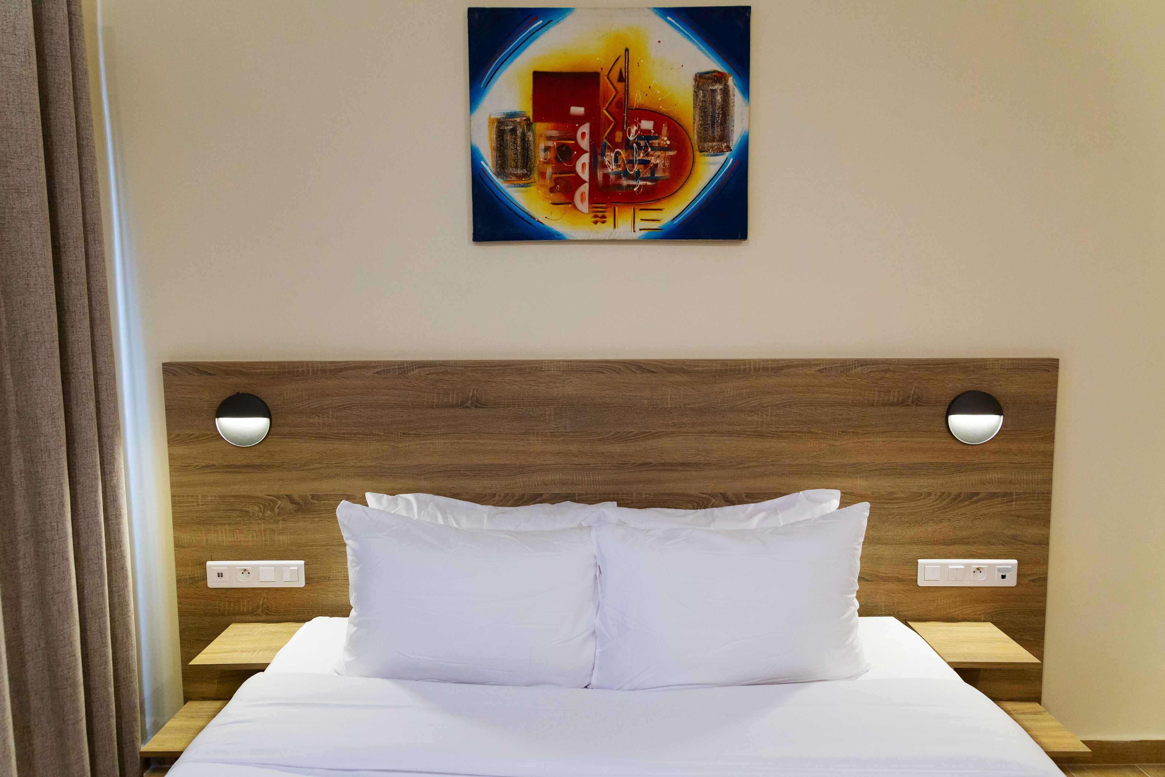 Een opgemaakt bed met witte lakens, een houten hoofdbord en twee nachtkastjes met lampen.