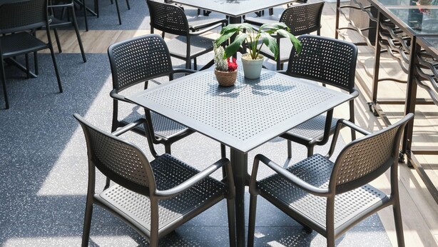 Een terras met tafels en stoelen, plantenpotten en een overdeeld gedeelte met uitzicht.