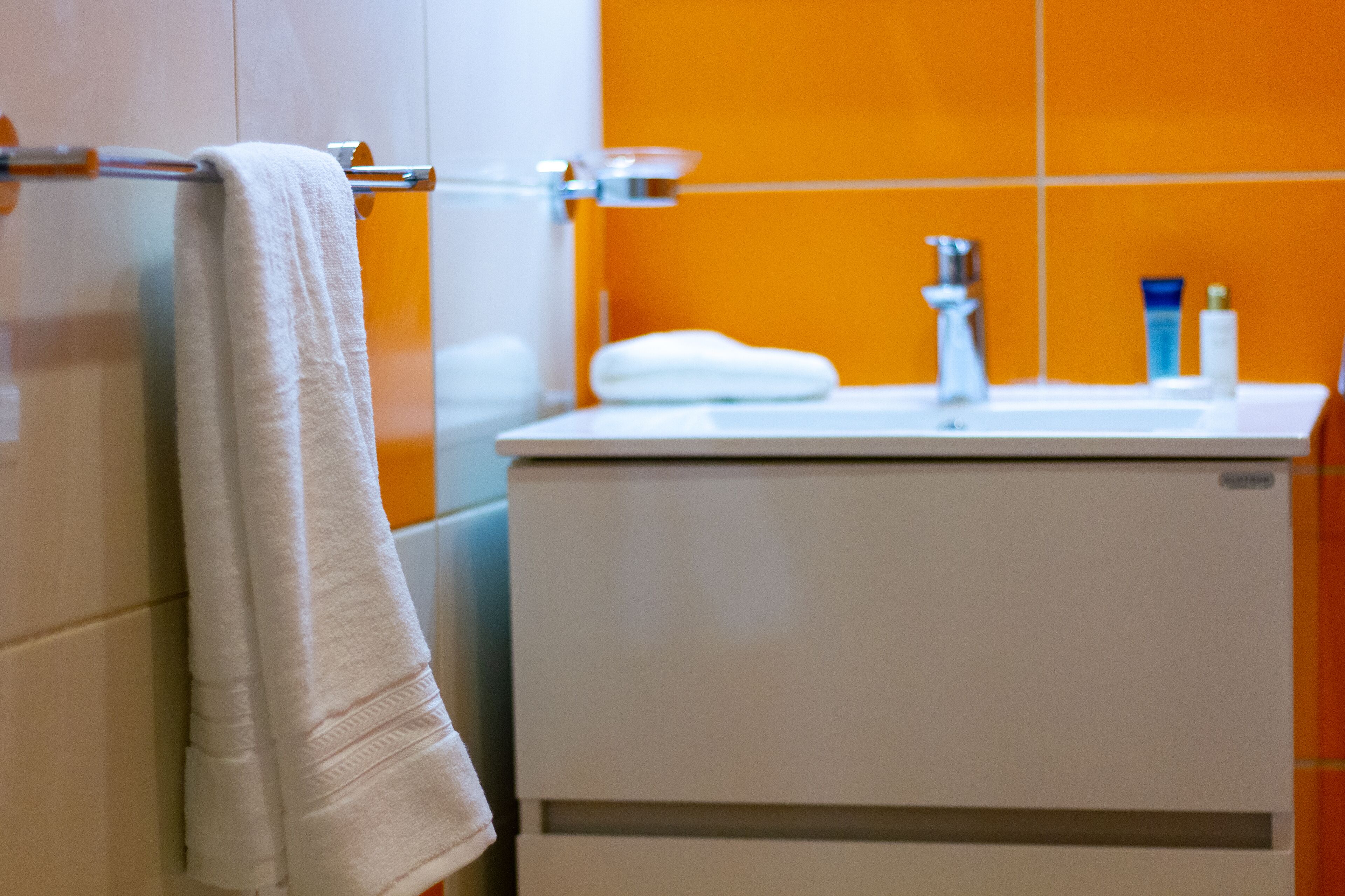 A bathroom with a white towel hanging on a glass towel rack, a white sink with a chrome faucet, and a white cabinet.