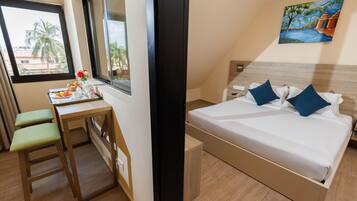 Habitación de hotel con cama, escritorio y ventana con vistas a palmeras.