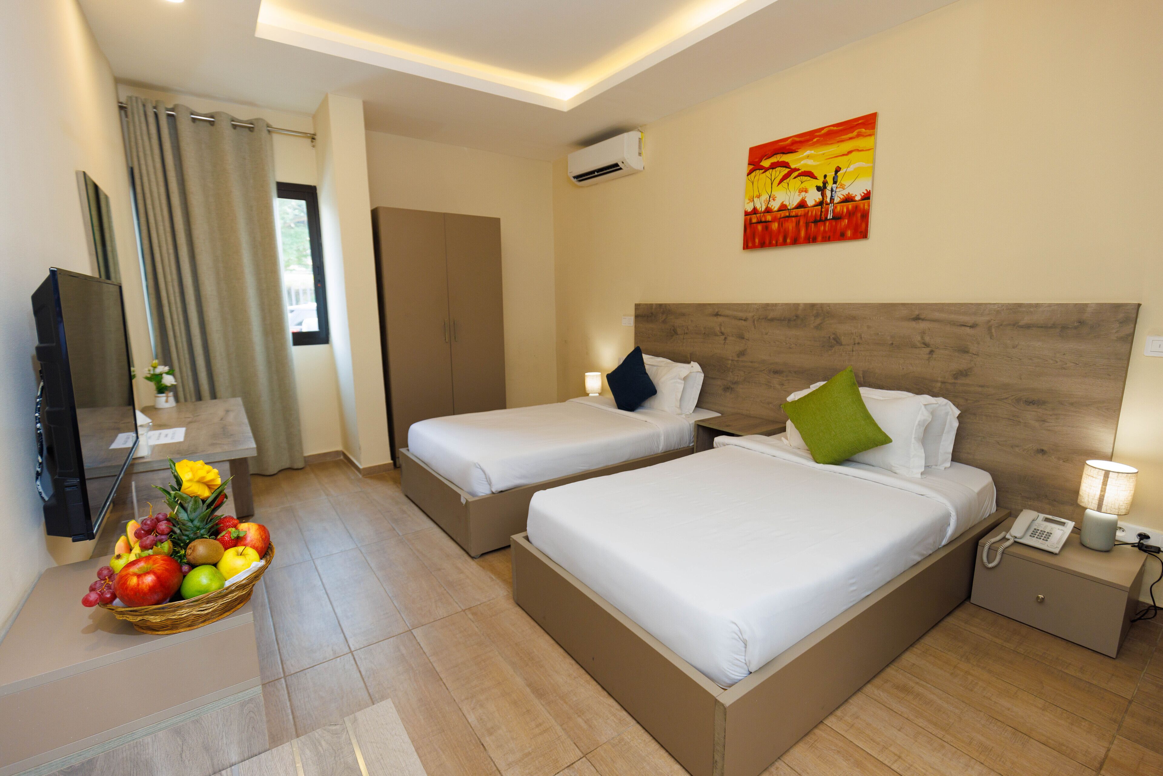 Une chambre d’hôtel avec deux lits, une télévision, un panier de fruits et un tableau au mur.