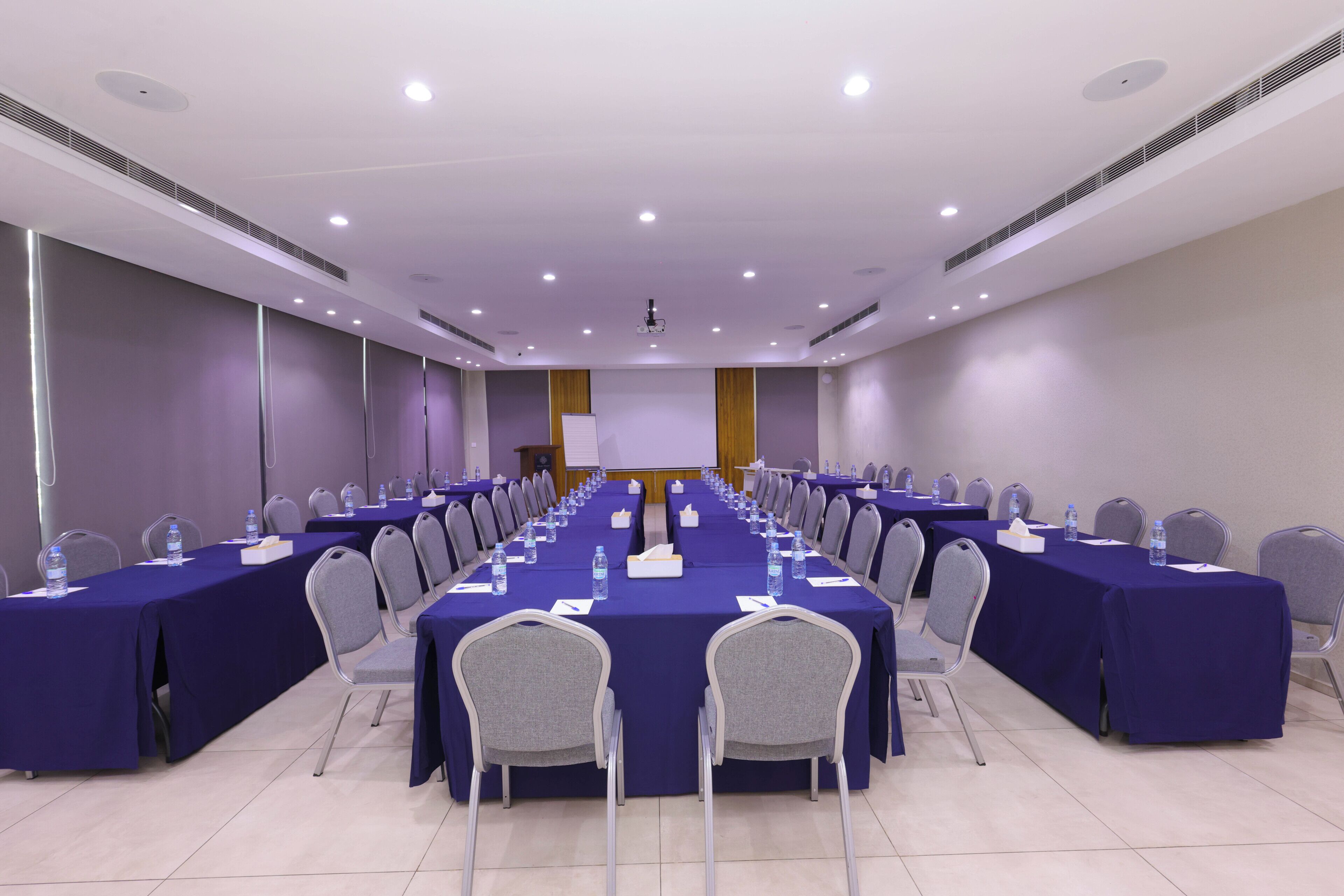 A conference room with a long table, chairs, water bottles, and a projector screen.