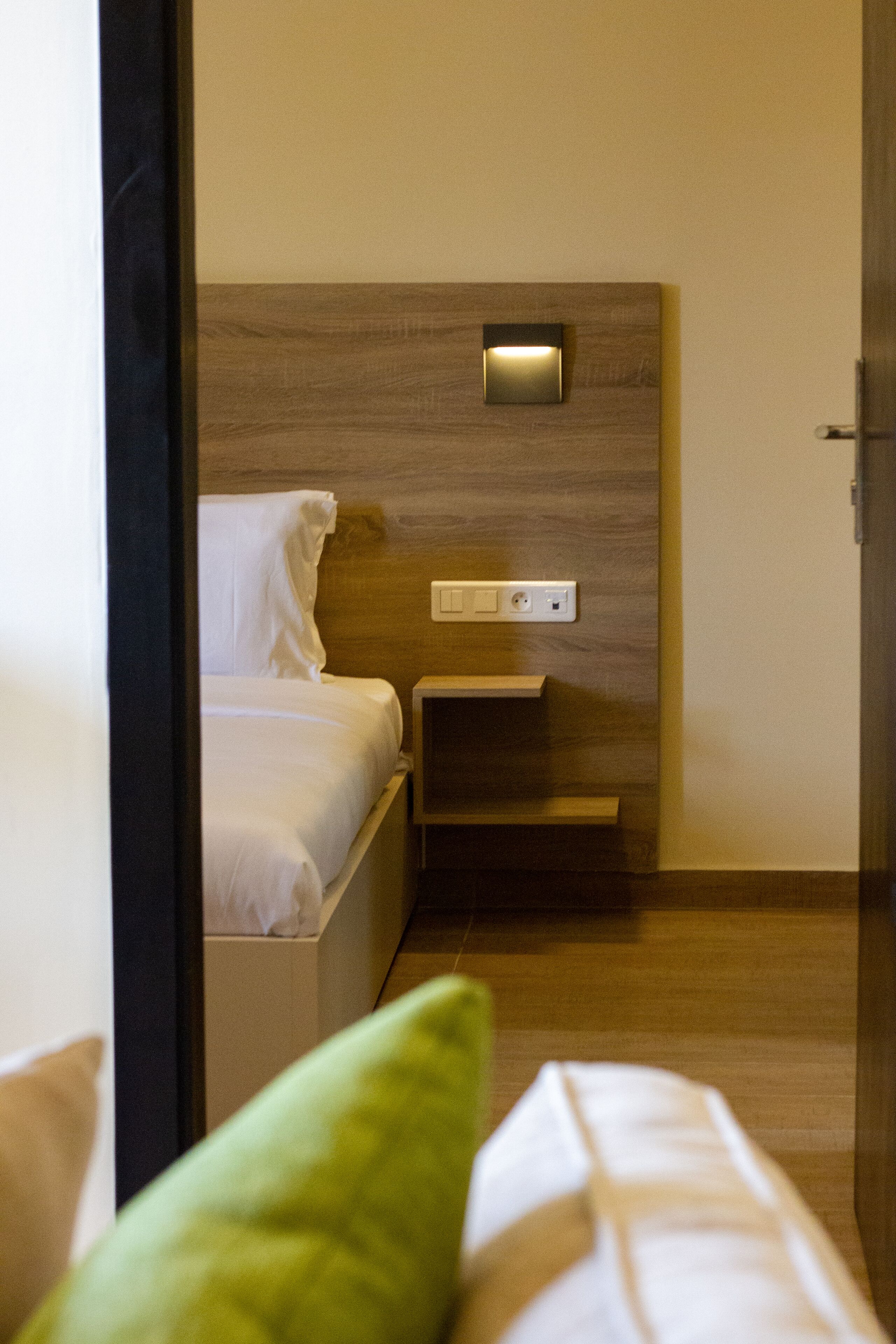 Hotellihuone, jossa on sänky, yöpöytä ja seinään kiinnitetty valaisin.