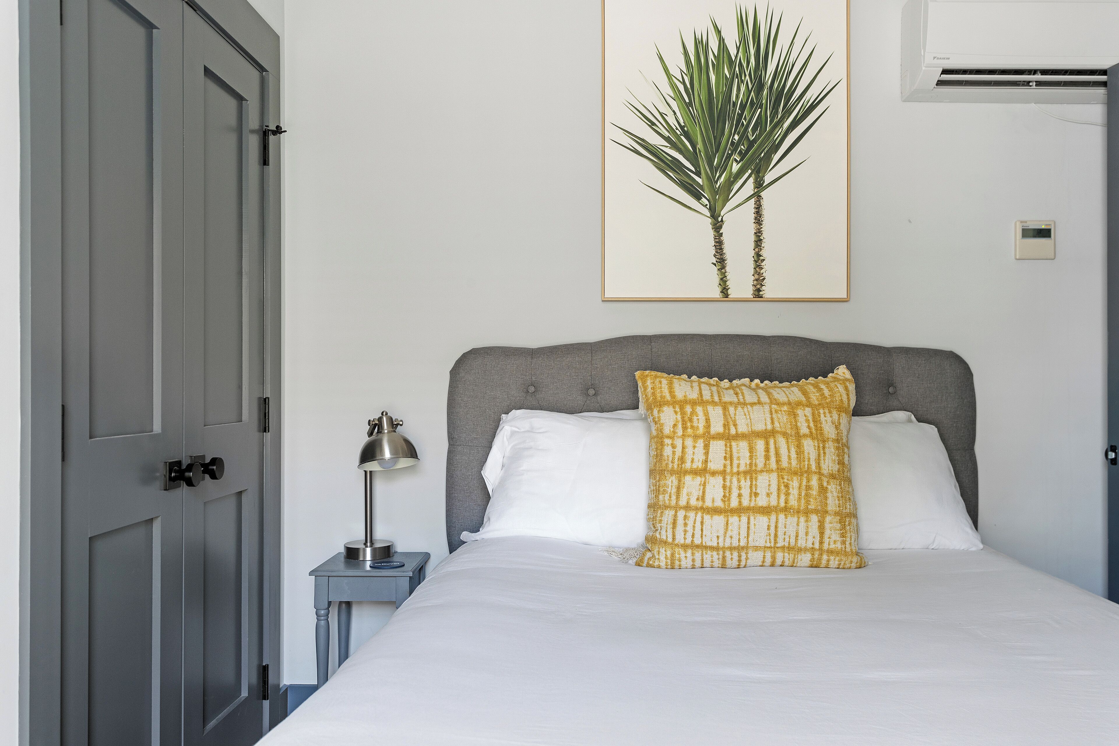 Une chambre à coucher avec un lit, une table de chevet, une lampe, une plante en pot et une porte.