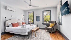 Quarto com cama, cadeira, escrivaninha e ventilador de teto.