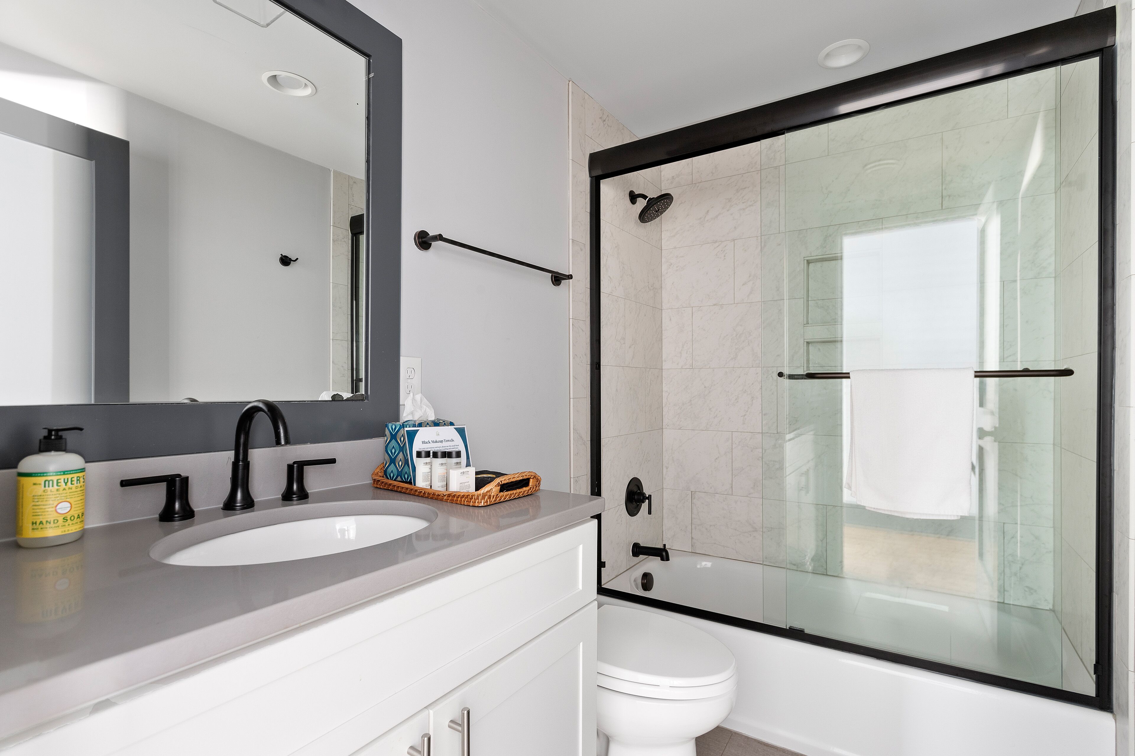 Un bany modern amb un mirall gran, un lavabo, un vàter i una zona de dutxa amb envàs de vidre.