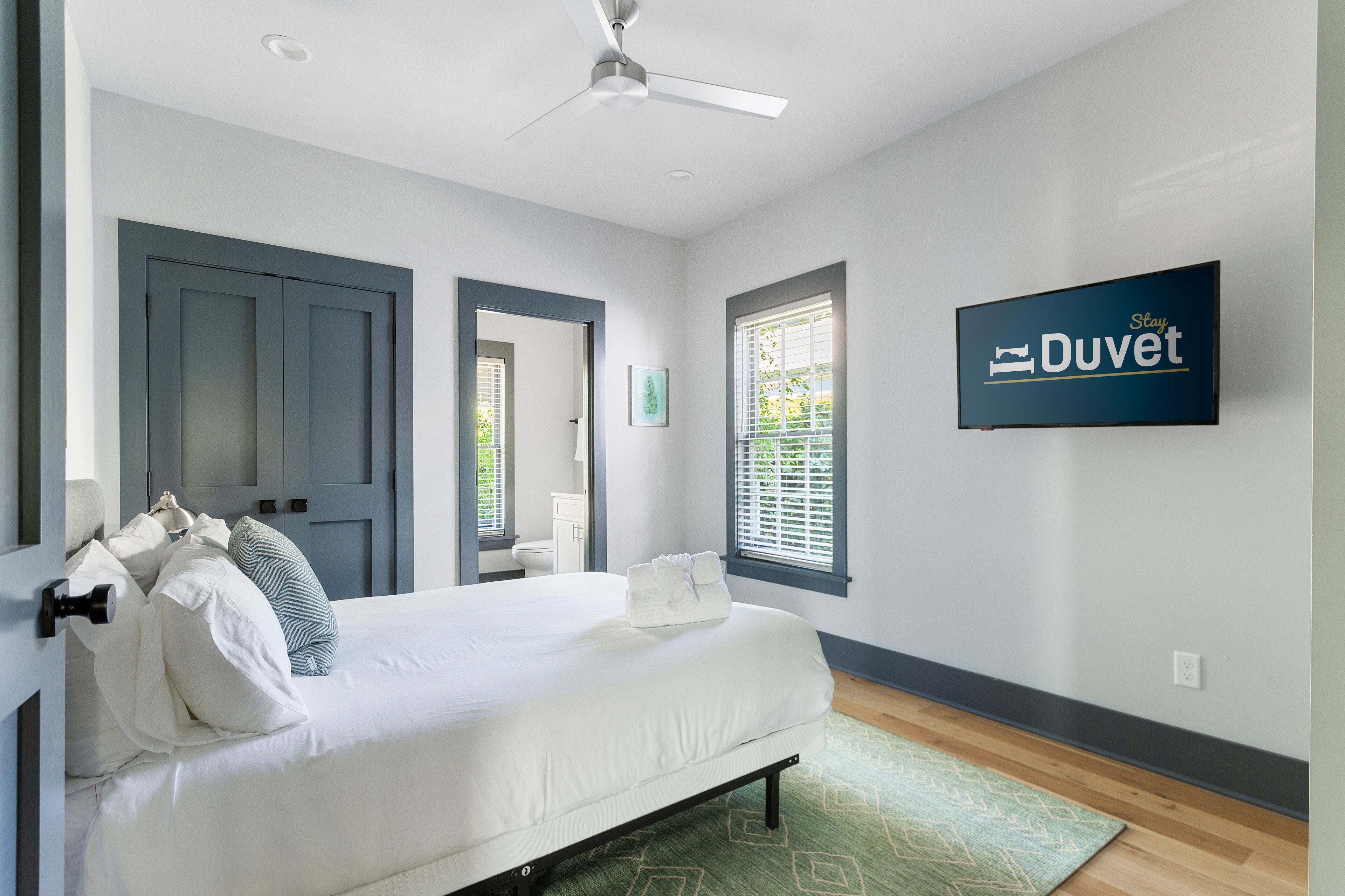 A bedroom with a bed, a ceiling fan, a TV, and a window with blinds.
