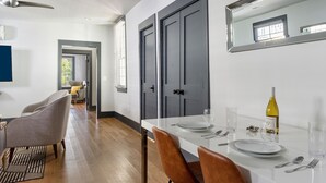 Uma zona de refeições moderna com uma mesa branca posta para dois, uma garrafa de vinho e um espelho grande na parede.