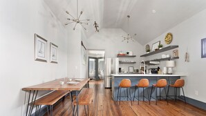 A modern kitchen with a central island, bar stools, and a dining area with a wooden table and benches. - Only 2 Blocks to King | The Gemstone (Suite B) (Charleston)