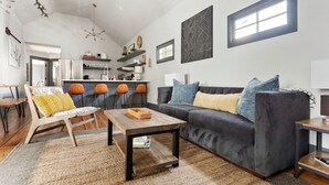 A modern living room with a dark grey sofa, wooden coffee table, and a light-colored rug. - Only 2 Blocks to King | The Gemstone (Suite B) (Charleston)