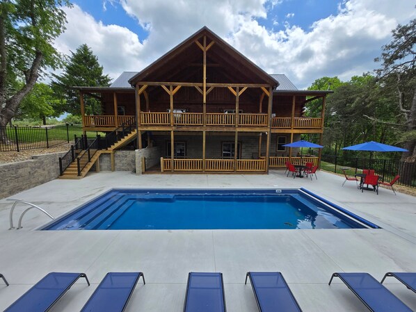 A two-story wooden lodge with a swimming pool and outdoor seating.