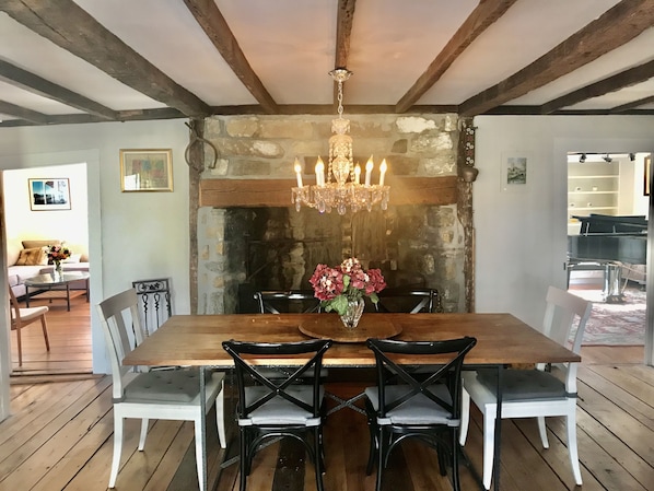 Une salle à manger avec une table en bois, des chaises noires, un lustre et une cheminée en pierre.