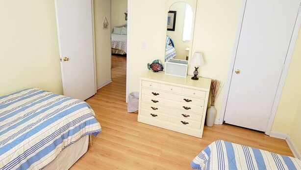 Una camera da letto con due letti, una cassettiera, uno specchio e una porta che dà su un'altra stanza.