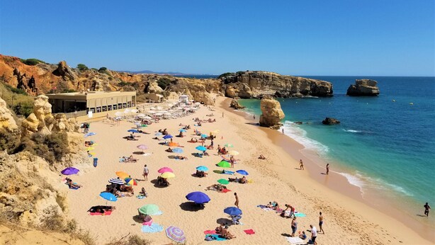 A beach with people sunbathing, umbrellas, and a building with a flag.