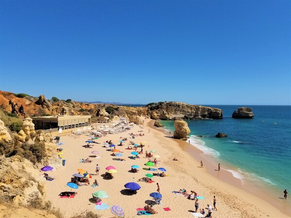 A beach with people sunbathing, umbrellas, and a building with a flag.