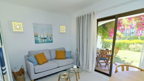 A living room with a sofa, a glass coffee table, and a view of a garden through a sliding door.