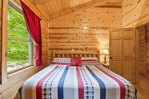 Ett sovrum i en stuga med träpanel, inrett med en säng, ett fönster med gardiner och en dörr.