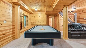A pool table in a wooden room with a staircase and a leather sofa. - Freedom Lodge | Sleeps 12 | 4BR + Loft | Hot Tub, Pool Table & Covered Decks (Rockbridge)