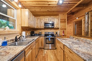 A compact kitchen with wooden cabinets, a stainless steel microwave, an oven, and granite countertops.