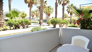 A balcony with a checkered table and chair, surrounded by palm trees and a white wall. - 1-bedroom Kos Olympia Apartment at Lambi Beach (Kos)