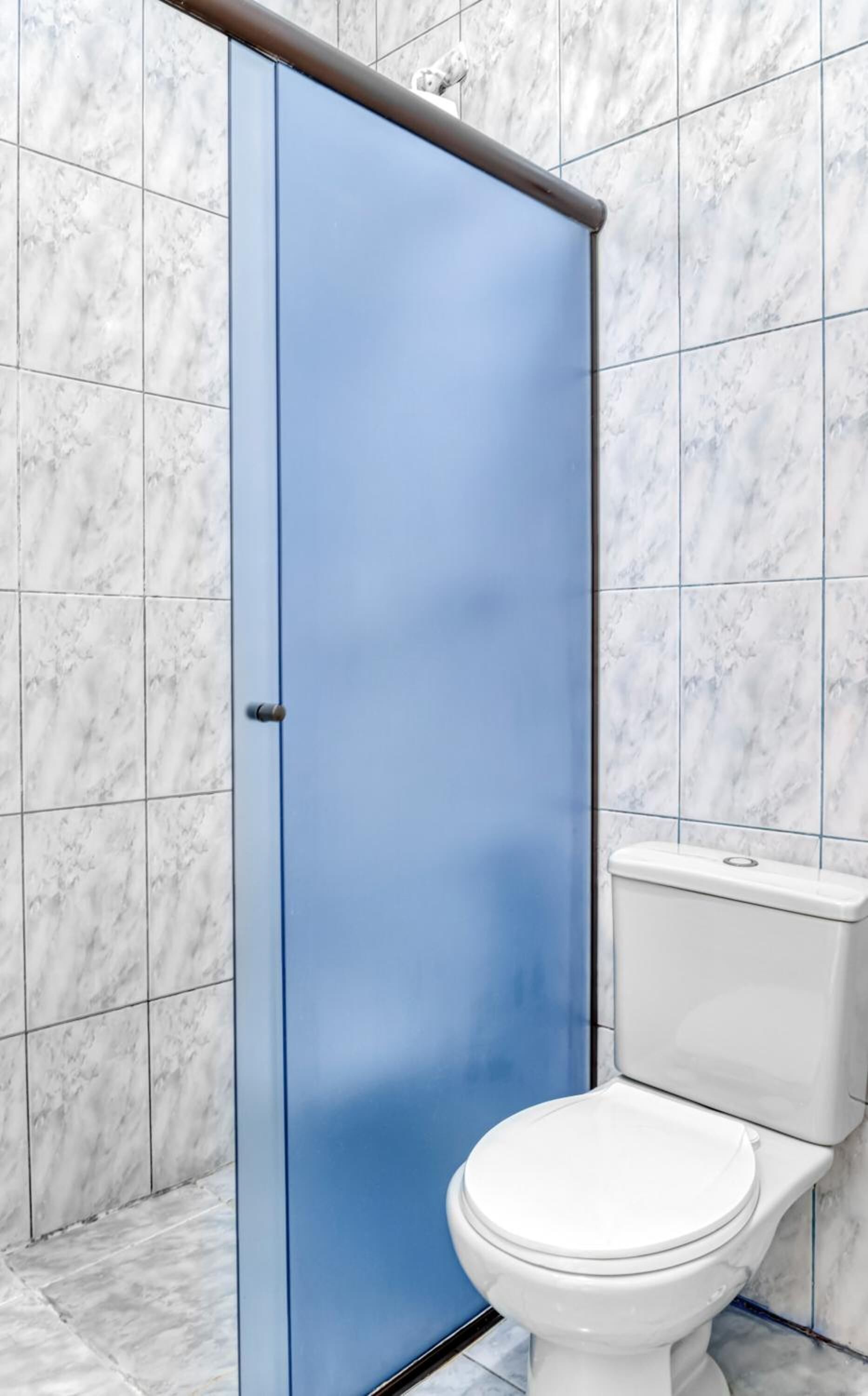 Un baño con puerta azul, inodoro blanco y azulejos de mármol.