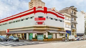 A hotel with a red and white facade, a visible entrance, and parked cars and motorcycles in front. - Hotel Urban Mooca (São Paulo)