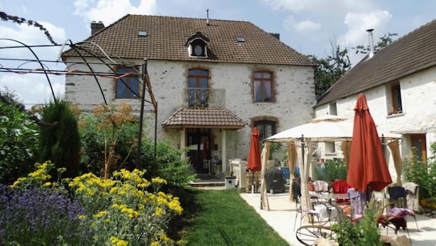 A two-story house with a tiled roof, a balcony, and a garden with yellow flowers. - A warm, 100% eco-responsible hotel to recharge your batteries (Morsains)