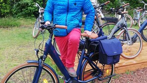 A person sitting on a bicycle with a blue bag attached, parked in front of a building with a brick facade. - A warm, 100% eco-responsible hotel to recharge your batteries (Morsains)