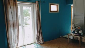 A room with teal walls, a checkered floor, a door with curtains, a small window, and a table with cups.