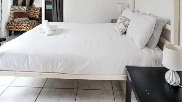 A bedroom with a bed, a nightstand, a lamp, a ceiling fan, and a 'Relax' sign on the wall.