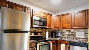 A modern kitchen with stainless steel appliances, wooden cabinets, and a tiled backsplash.