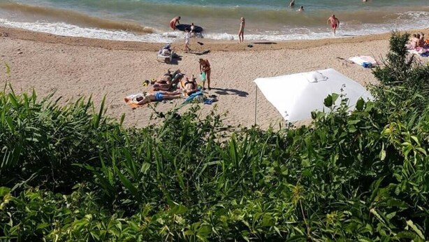 Una playa con gente tomando el sol y nadando, un barco en el agua y montañas al fondo.