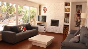 A modern living room with two grey sofas, a white coffee table, a flat-screen TV, and a fireplace. - LA RESTONICA (Fréjus)