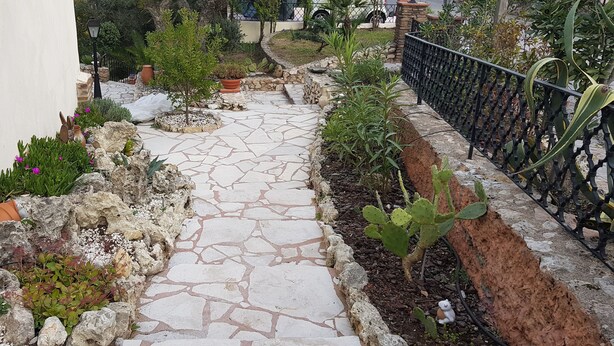 A stone pathway leading through a garden with various plants and a metal fence on one side. - LA RESTONICA (Fréjus)