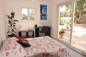 A bedroom with a bed, a desk, and a chair. There is a window with a view of the outside.