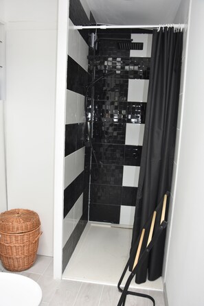 A shower area with black and white checkered tiles, a wicker basket, and a black shower curtain.