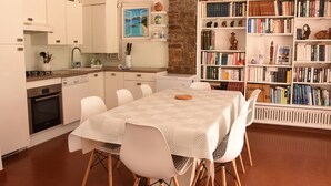 A modern kitchen with white cabinets, a dining table with chairs, and a bookshelf filled with books. - LA RESTONICA (Fréjus)