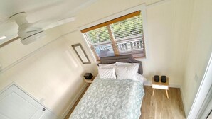 A bedroom with a bed, a window with blinds, a bedside table, and a nightstand.