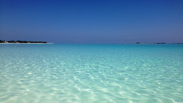 A clear turquoise sea with a sandy beach and distant land.